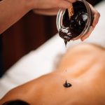 Beautician Applying Dark Cocoa Paste on Woman’s Back.