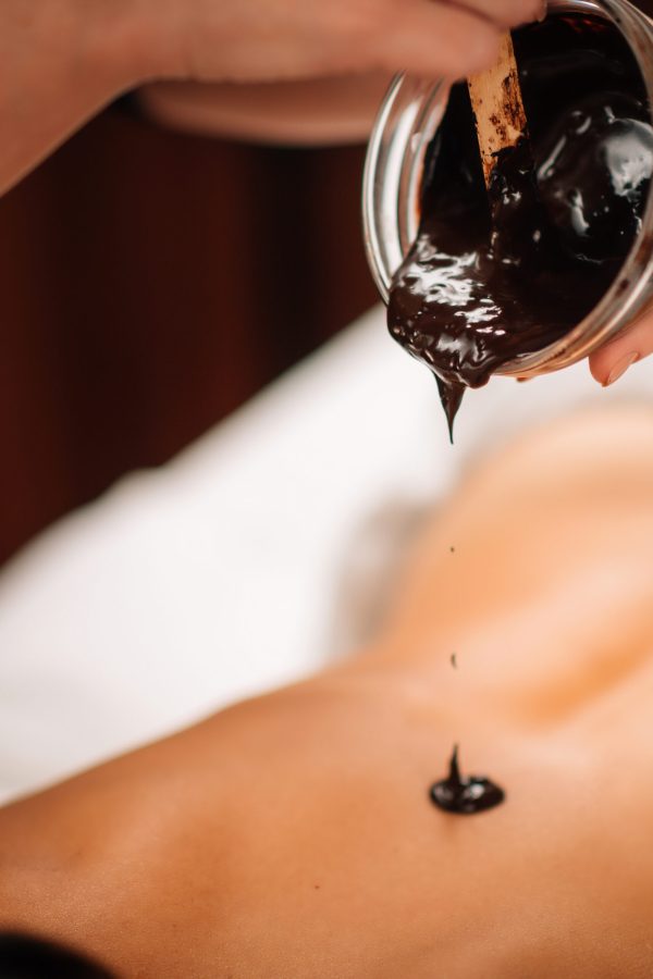 Beautician Applying Dark Cocoa Paste on Woman’s Back.