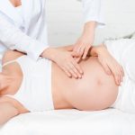 Cropped view of masseur doing belly massage to pregnant woman on massage table