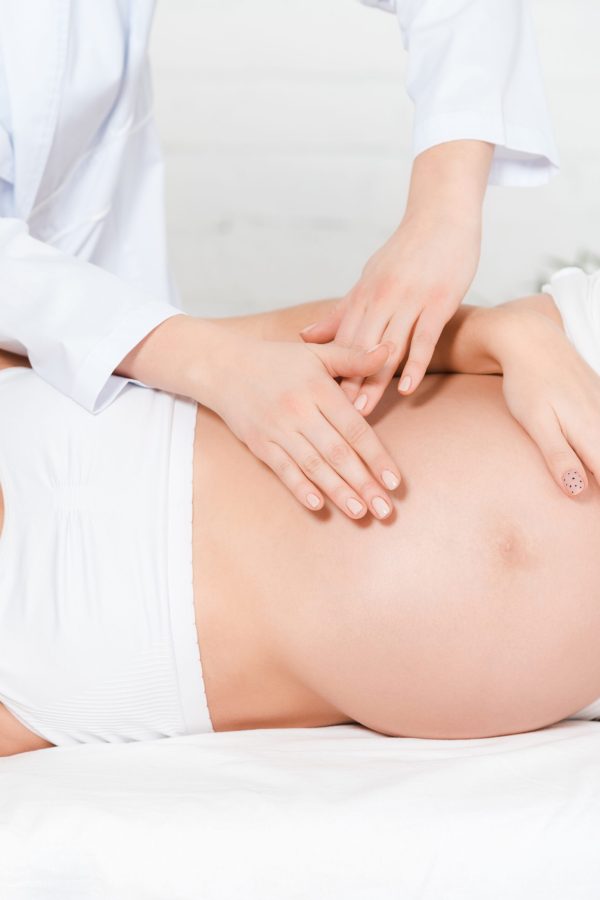 Cropped view of masseur doing belly massage to pregnant woman on massage table