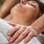 Thai Healing Massage - Energy work between Practitioner and Client. Traditional Thai massage therapist holding hands on the female patient's shoulder.