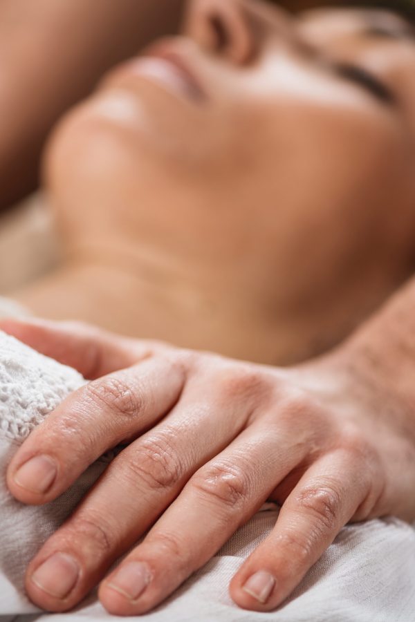 Thai Healing Massage - Energy work between Practitioner and Client. Traditional Thai massage therapist holding hands on the female patient's shoulder.